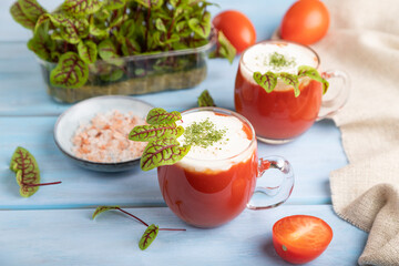 Tomato juice with sorrel, salt and sour cream in glass on blue wooden background. Side view, selective focus.