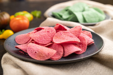 Green and red potato chips with herbs and tomatoes on black concrete background. Side view, close up, selective focus.
