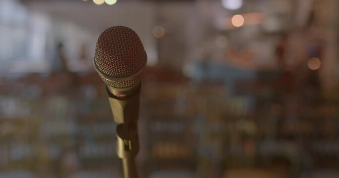 Device sitting voice transmitting information wide audience. Close-up microphone preparation performance. Against background movement person in bokeh. Waiting for audience and guest to arrive.