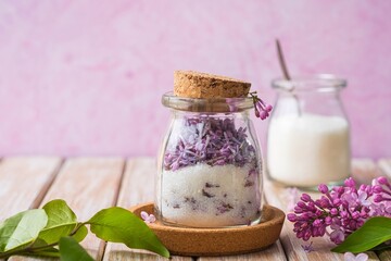 Flavored sugar with lilac flowers in a transparent glass jar on a wooden background. The use of edible wild plants and flowers in cooking.