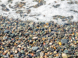 Wave on a pebbly shore. Sea foam.  Beautiful pebble beach. Close-up of the coastline