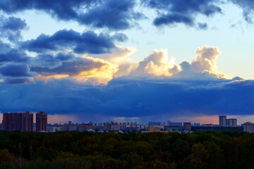 A blue cloud pours rain on the city from above illuminated by the sun