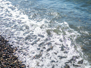 Fototapeta na wymiar Wave on a pebbly shore. Sea foam. Beautiful pebble beach. Close-up of the coastline