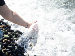 A hand with a bracelet made of stones reaches for the water. Sea wave and female hand. Feel the wave. Pebble beach.
