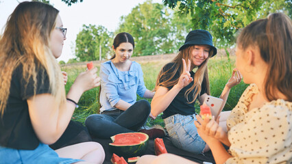 Friends have fun eating watermelon outside the city at a picnic.