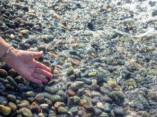 The hand reaches for the water. Sea wave and female hand. Feel the wave. Pebble beach.