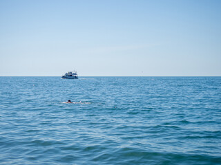 The man swims towards the boat. Seascape. Resort place. Place for rest.