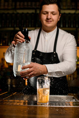man bartender holds a siphon and splashes on glass with a cold cocktail