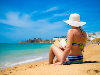 Fototapeta na wymiar Woman sitting on beach reading book 