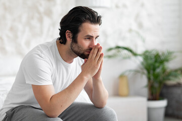 Unhappy young man sitting on bed alone, copy space