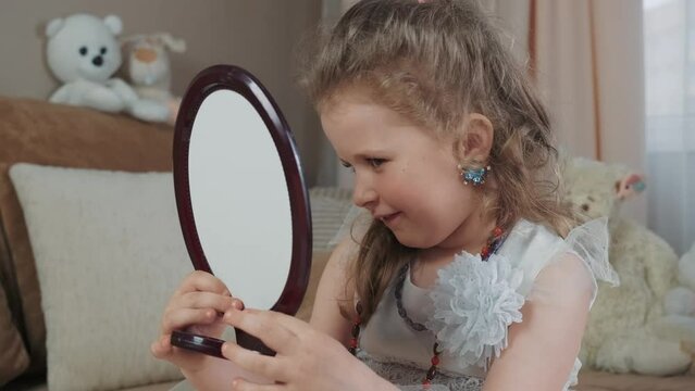 Funny little baby girl trying on her mom's earrings. Funny baby is putting on beauty, trying on jewelry, merrily admiring herself in the mirror. The daughter is getting ready for a children's party