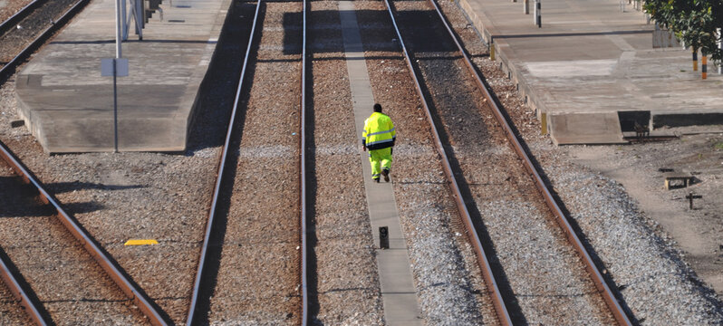 Funcionário de companhia de comboios a andar a pé com um fato de alta visibilidade, corredor no meio does trilhos dentro de uma estação