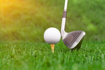 Golf club and ball on green grass ready to be struck on golf course background, evening time.