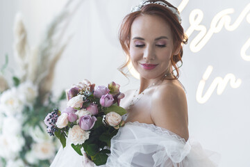 Beautiful attractive caucasian young woman in a white wedding dress with a bridal flower bouquet. Smiling