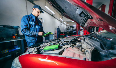 Car service electrician or mechanic uses a tablet computer with futuristic interactive diagnostics software. Inspecting the vehicle in order to find broken components in the engine bay of modern car
