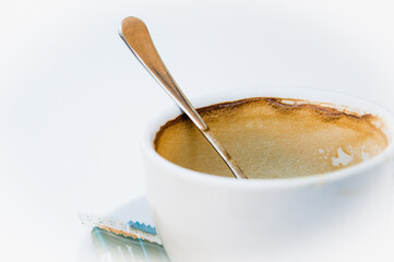 Taza vacía de café con cuchara, sobre plato con una galleta empaqueta y fondo blanco aislado.