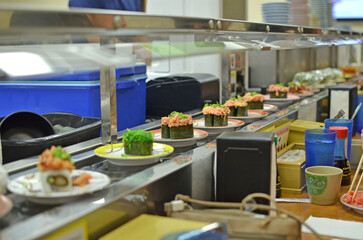 Plates of spicy tuna sushi and other varieties during a quick lunch on a conveyor belt at a kaitenzushi style restaurant