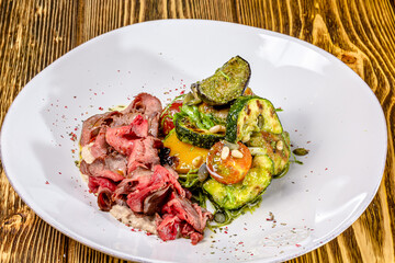 Sliced rare roast sirloin of beef with roasted vegetables on rustic wooden background