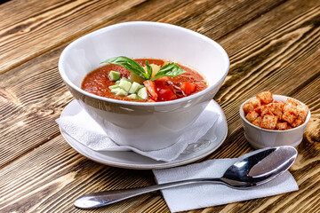 Raw tomato soup, typical food of Spain, served in white bowls with pieces of tomato, cucumber and paprika. Wooden background