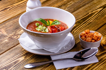 Raw tomato soup, typical food of Spain, served in white bowls with pieces of tomato, cucumber and paprika. Wooden background