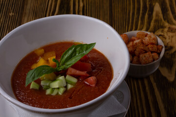 Raw tomato soup, typical food of Spain, served in white bowls with pieces of tomato, cucumber and paprika. Wooden background