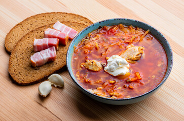 Ukrainian traditional cuisine. Red borscht with chicken and sour cream in a blue plate on a wooden background
