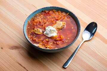 Ukrainian traditional cuisine. Red borscht with chicken and sour cream in a blue plate on a wooden background