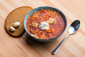 Ukrainian traditional cuisine. Red borscht with chicken and sour cream in a blue plate on a wooden background