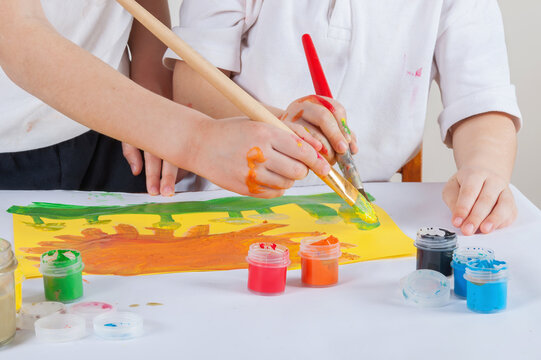 Two children are holding brush for painting. They are trying to draw a common picture (concept: teamwork)