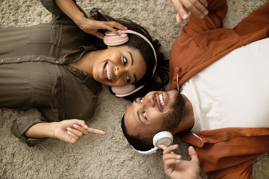 Happy African American Couple Listening Music Wearing Earphones Lying Indoor