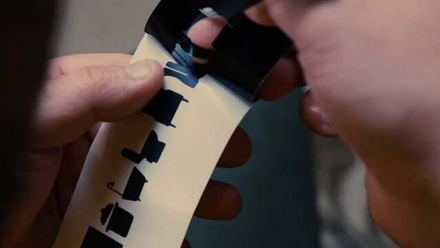Close-up time-lapse of a man's hands tearing off excess paper from a sticker at his work during the day.