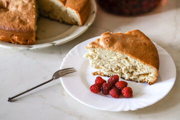 Piece of the homemade apple pie on the white plate served with some raspberries