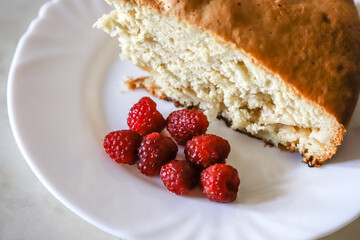 Piece of the homemade apple pie on the white plate served with some raspberries