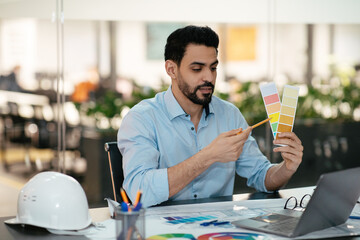 Serious young islamic male engineer designer with beard shows color palettes in laptop in office
