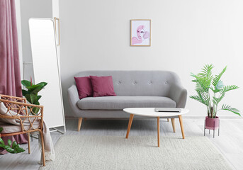 Interior of modern living room with comfortable sofa, mirror, table and houseplants near light wall