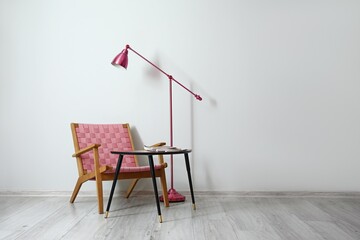 Comfortable armchair, table and floor lamp near light wall in room