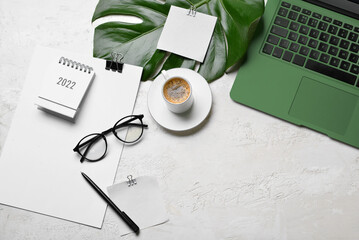 Laptop, cup of coffee, eyeglasses, stationery and tropical leaf on light background