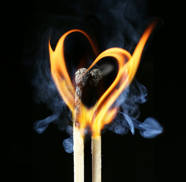 Two burning matches with flame in shape of heart on dark background