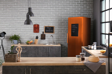 Interior of modern comfortable kitchen with orange fridge near brick wall