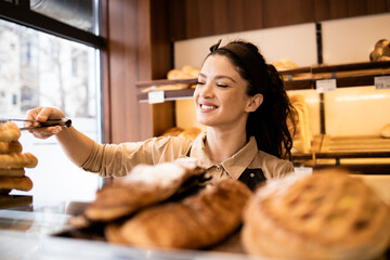 Woman working in bakery shop and selling delicious fresh pastry and bread.