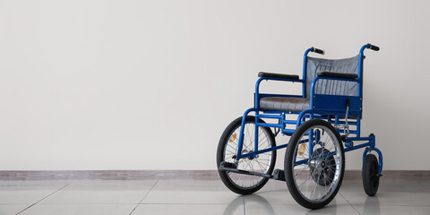 Fototapeta na wymiar Empty wheelchair near light wall