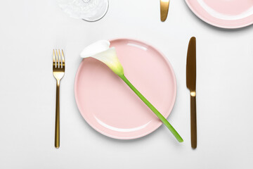 Beautiful table setting with golden cutlery and calla lily on white background, closeup