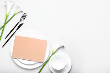 Beautiful table setting with blank card and calla lilies on white background