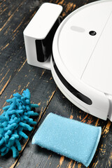 Robot vacuum cleaner and cleaning supplies on dark wooden background, closeup