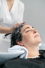 the cosmetologist washes the girl's head with shampoo for further procedures. black hair. plus size.