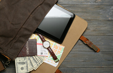 Bag with guide's belongings and tablet computer on dark wooden background