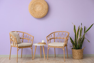 Wicker chairs and table near violet wall in room interior