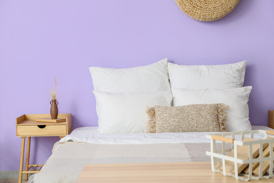 Comfortable bed near violet wall in bedroom