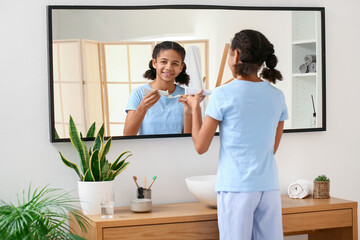 Fototapeta na wymiar African-American teenage girl applying tooth paste onto brush in bathroom