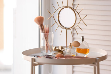 Holder with makeup brushes, cosmetic products and mirror on table near window